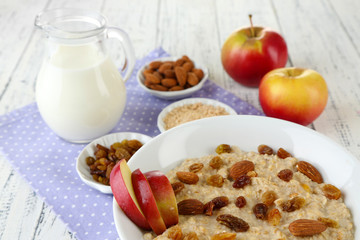 Tasty oatmeal with raisins and apples on wooden table