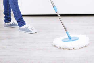 Woman with mop cleaning wooden floor from dust