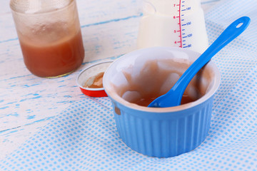 Baby bottle with milk and dirty bowl on wooden table