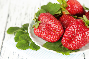 Strawberries with leaves on plate, on wooden background