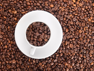 A white cup with many coffee beans on coffe background