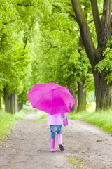 little girl wearing rubber boots with umbrella in spring alley