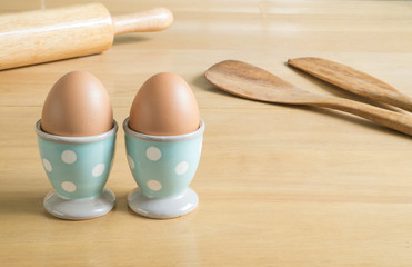 Two eggs in blue polka dot egg cups and baking utensils