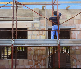 Worker on scaffold building masonry clay blocks