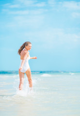 Fototapeta na wymiar Cheerful young woman in swimsuit walking on sea shore