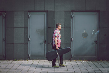 Man in short sleeve shirt walking with guitar case - obrazy, fototapety, plakaty