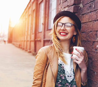Cheerful woman in the street drinking morning coffee in sunshine