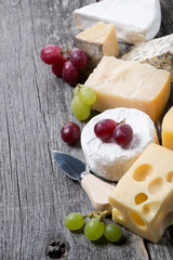 assortment of cheeses and grapes on a wooden board