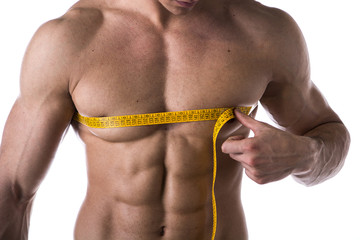 Muscular shirtless young man measuring chest with tape measure