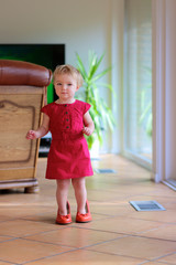 Adorable toddler girl walks indoors in mom's red shoes
