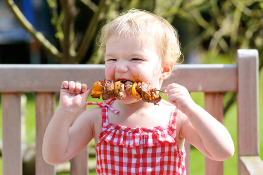 Funny Toddler Girl In Eating Meat From Bbq In Summer Garde