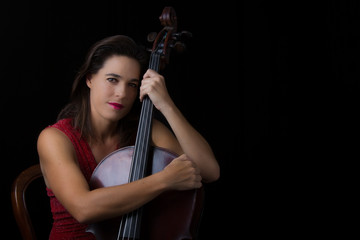 Beautiful brunette holding cello with selective light in red dre