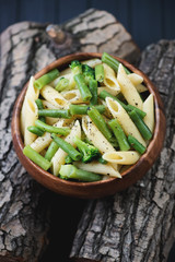 Penne with beans and broccoli on wooden logs, studio shot