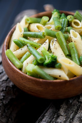 Close-up of penne pasta with beans and broccoli in a wooden bowl
