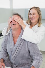 Smiling woman covering man's eyes in kitchen
