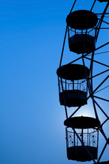 Ferris wheel silhouette in blue sky.