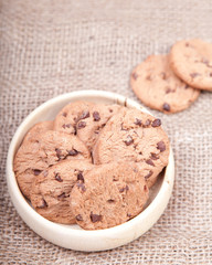 Chocolate chip cookies in a wooden bowl on a hessian background
