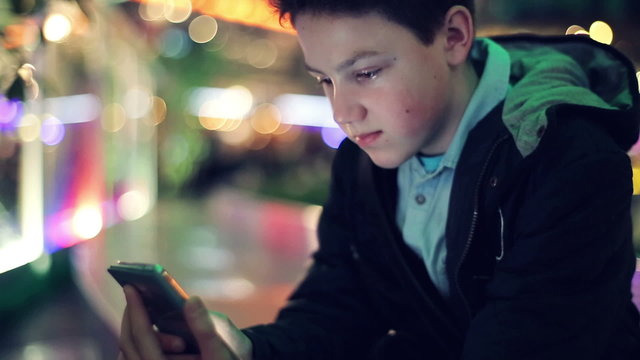Young teenager texting on smartphone in the city at night