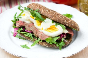 Sandwich with grilled beef steak, eggs, arugula, rye bread