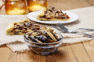 Bowl of raw mushrooms and mushroom galette in the background