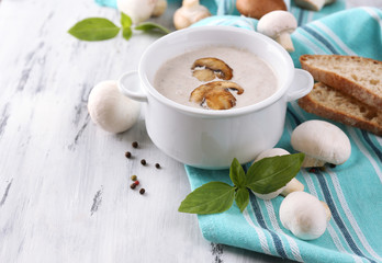 Mushroom soup in white pot, on napkin,  on wooden background