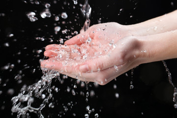 Fototapeta premium Human hands with water splashing on them on black background