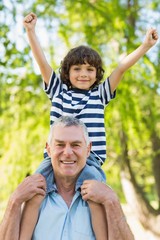 Grandfather carrying son on shoulders at park