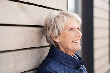 entspannte seniorin lehnt an einer holzwand