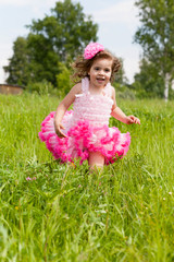 Fototapeta na wymiar cheerful girl in a pink dress runs on a grass