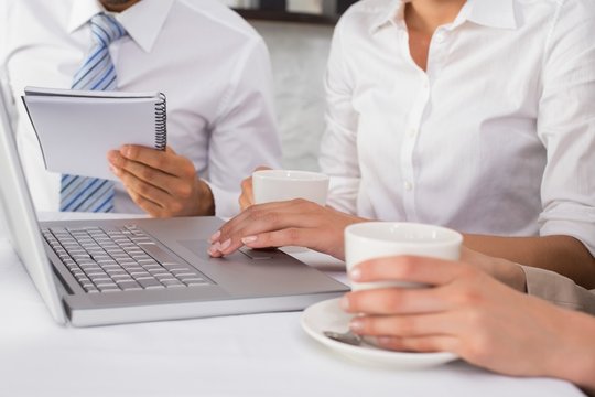 Mid section of three business people using laptop
