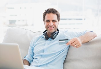Fototapeta premium Happy handsome man sitting on sofa online shopping with laptop