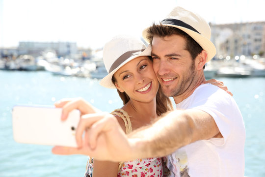 happy couple of tourists taking pictures with smartphone