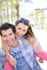 Fototapeta na wymiar Cheerful girl on boyfriend's back showing thumbs up