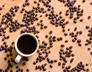 Cup of black coffee and coffee beans on wooden background.