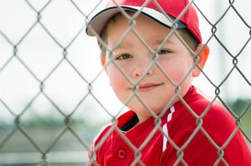 Young baseball player in uniform sitting in dugout