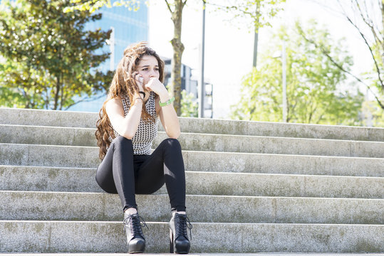 Pensive Young Woman Talking By Phone And Sitting On Stairs.