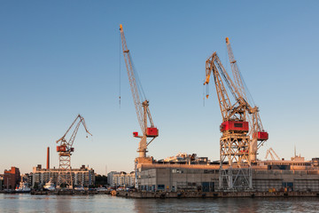 Fototapeta na wymiar sea port cranes with blue cloudy sky in background and water in