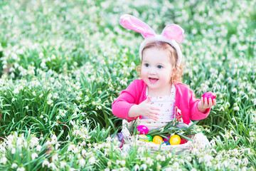 Cute toddler girl in bunny ears in meadow of flowers Easter egg