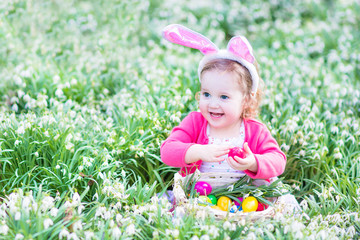 Beautiful toddler girl in bunny ears playing with Easter eggss