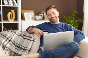 Smiling man with laptop and credit card on sofa