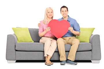 Obraz premium Young couple holding big red heart seated on sofa