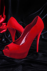Female red high-heeled shoes over black background.