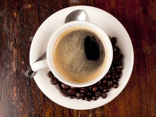 Top view of a cup of dark roasted coffee with coffeebeans