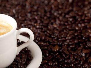Fresh cup of dark roasted coffee with coffeebeans in the backgro