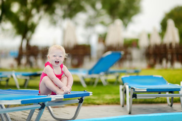 Toddler girl sitting on a sunbed by a pool