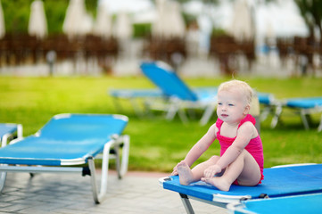 Toddler girl sitting on a sunbed by a pool