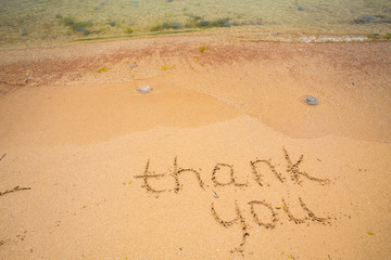 Thank you written in the sand on beach.
