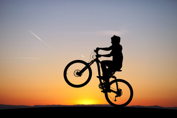 silhouette of boy riding his mountain-bike in sunset