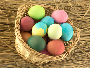 Fototapeta na wymiar Color Easter eggs in brown basket on straw closeup