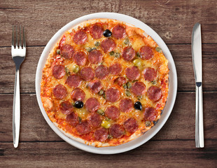 Italian salami pizza top view on plate with fork and knife